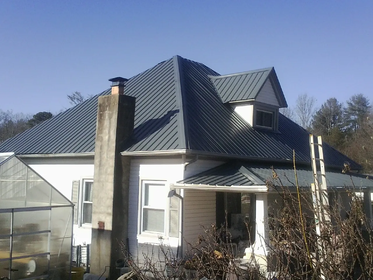 Dark blue standing seam metal roof on a white farmhouse with dormer — Slate & Tile Roof Repair by Roofing Brothers in Luttrell