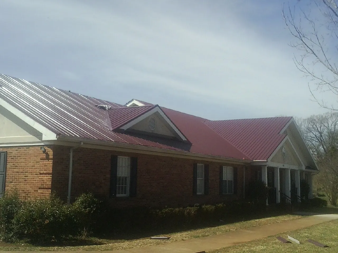 Red metal roof with gabled entries on a long brick building, from a Hail Damage Roof Repair job in Luttrell
