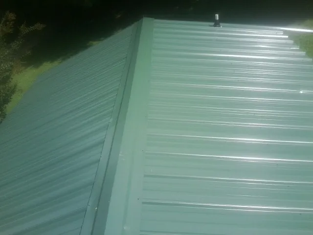 New green metal panels meeting at the ridge of a roof — Flat Roof Repair work by our crew in Luttrell