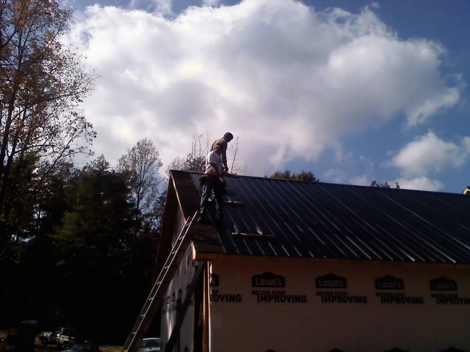 Roofer fastening dark metal panels high against a cloudy sky, from a Roof Inspection job in Luttrell