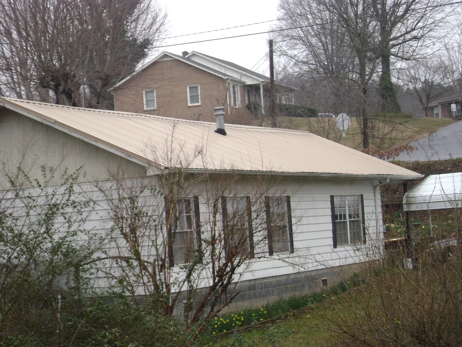Tan metal roof on a white sided house set into a hillside — Commercial Roofing by Roofing Brothers in Luttrell