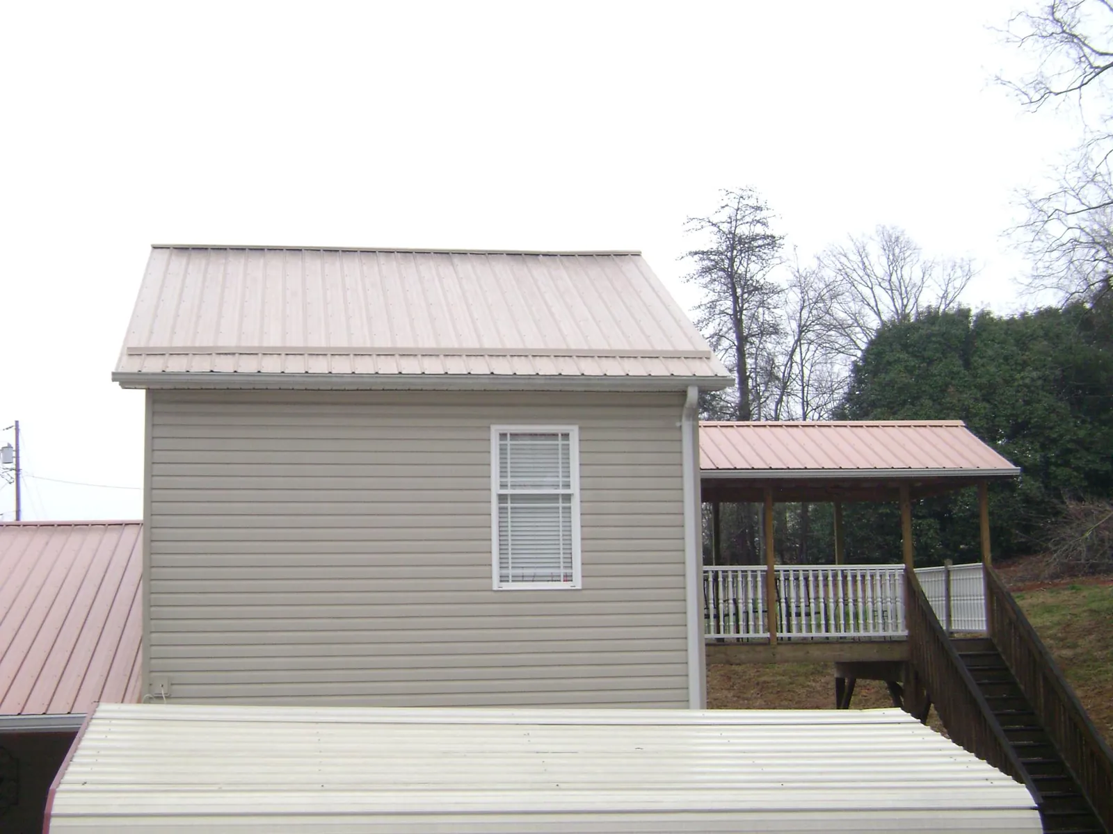 Tan metal roofs on a two story addition and attached porch, from a Roof Replacement job in Luttrell